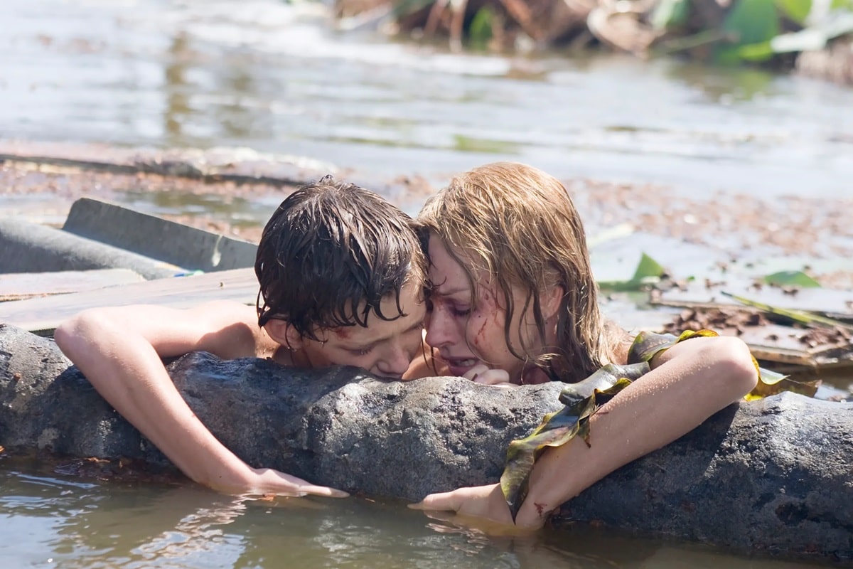 Tom Holland y Naomi Watts agarrados de un tronco en medio de un tsunami en la película Lo imposible