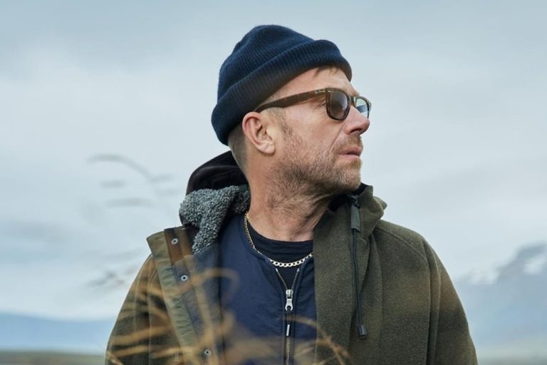 Damon Albarn con un gorro azul y una campera, mirando hacia un costado