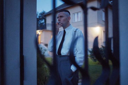 Christian Friedel fuma mientras mira a través de la puerta de su casa